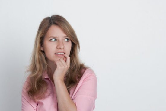 Blond woman biting her fingernail looking hesitant