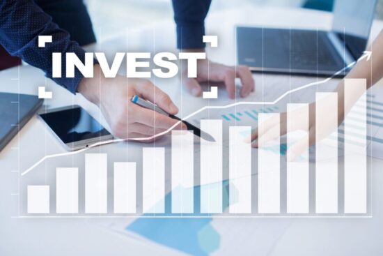 Someone in in a business suit holding a pen in his hand. Overlayed are rising bars and the word "Invest" above them