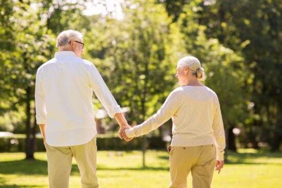 A retired man and woman walking away from the camera holding hands.