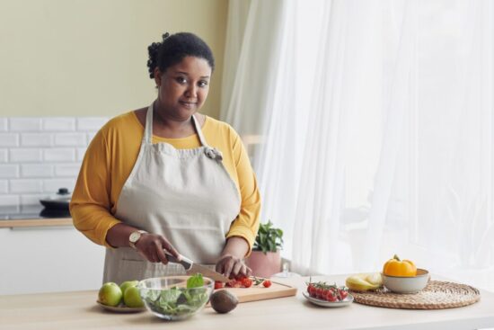 African American woman wearing an apron and cutting vegetables in her kitchen