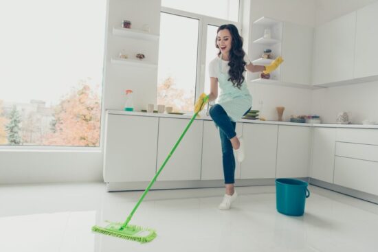 Woman happily mopping the floor in a white kitchen