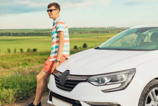 Teen boy wearing shorts sitting on the hood of his white car