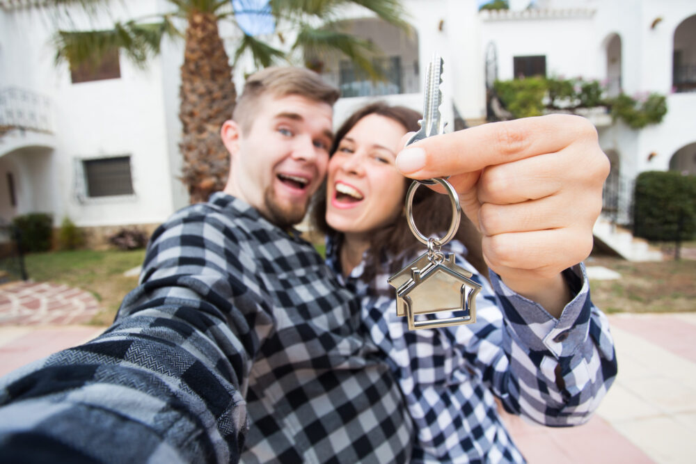 can i afford a second home - New Home, real estate and moving concept - Funny young couple showings keys from new house