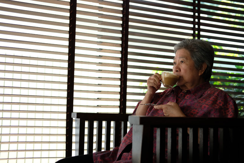 asian elderly woman sitting and resting in cafe holding cup of cappuccino coffee. Elder senior lady in restaurant