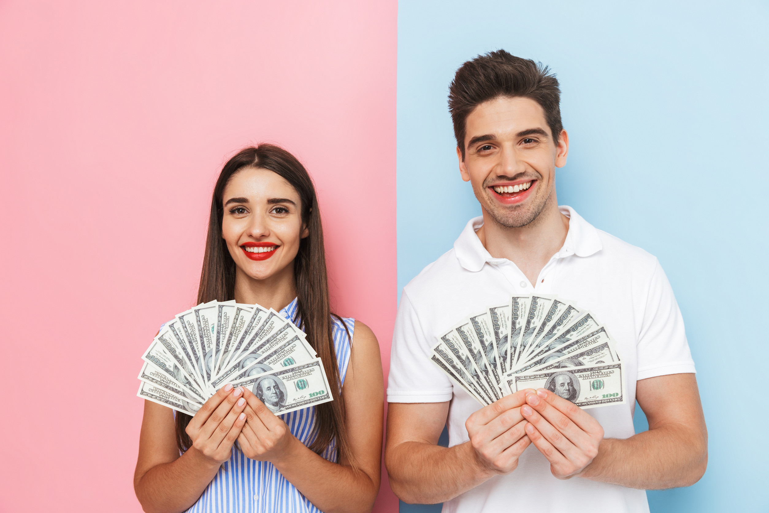 Excited young couple standing isolated over two colored background, showing money banknotes