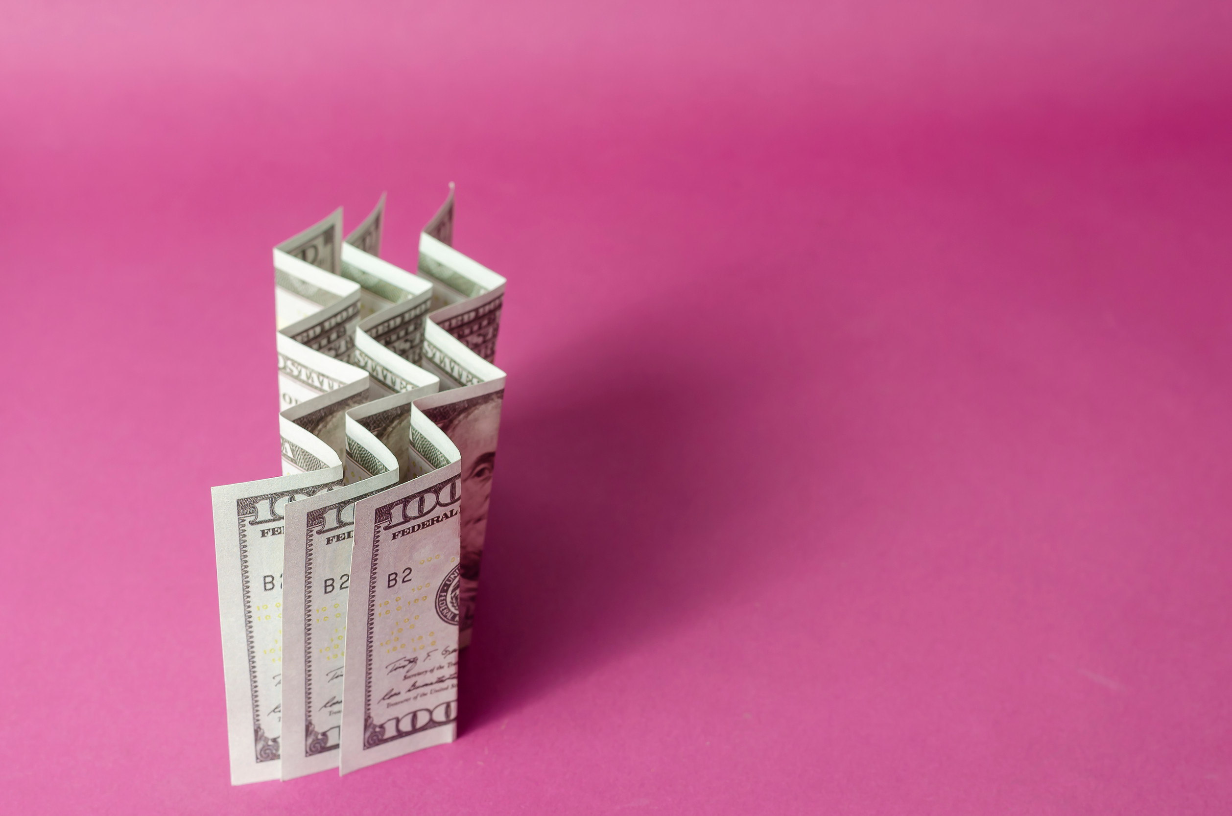 Accordion folded hundred dollar bills on a pink background. Abstract background with three banknotes.